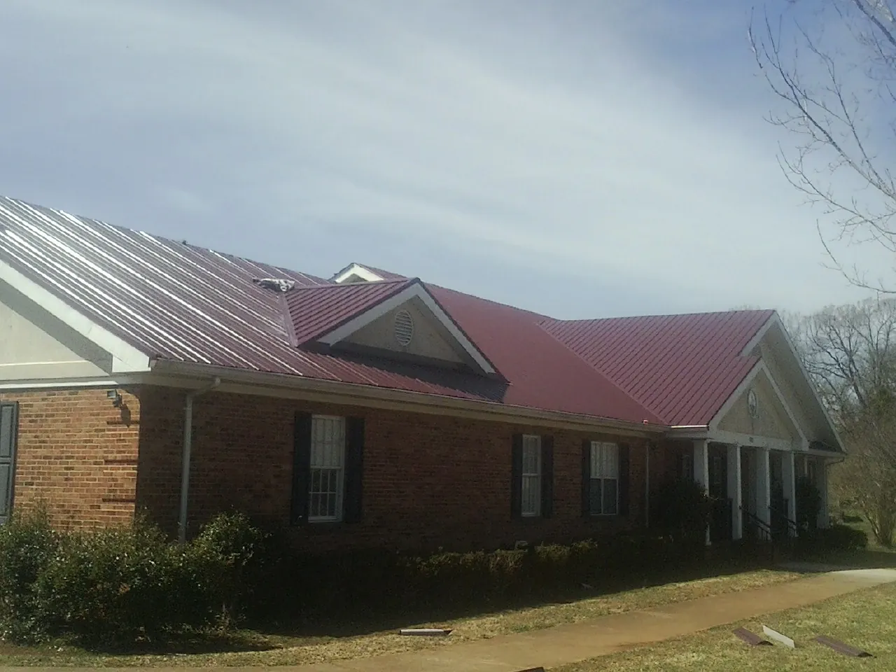 Red metal roof with gabled entries on a long brick building, from a Hail Damage Roof Repair job in Los Gatos